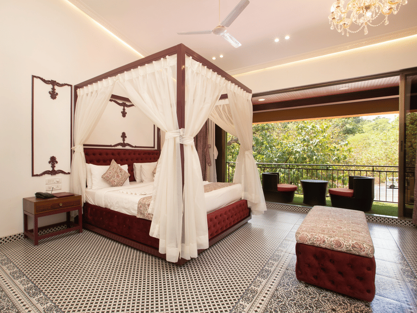 The luxurious Royal Suite at Zara's Resort, Khandala, featuring a 4-poster bed at the centre  with draped fabric, facing an open balcony with greenery visible beyond.