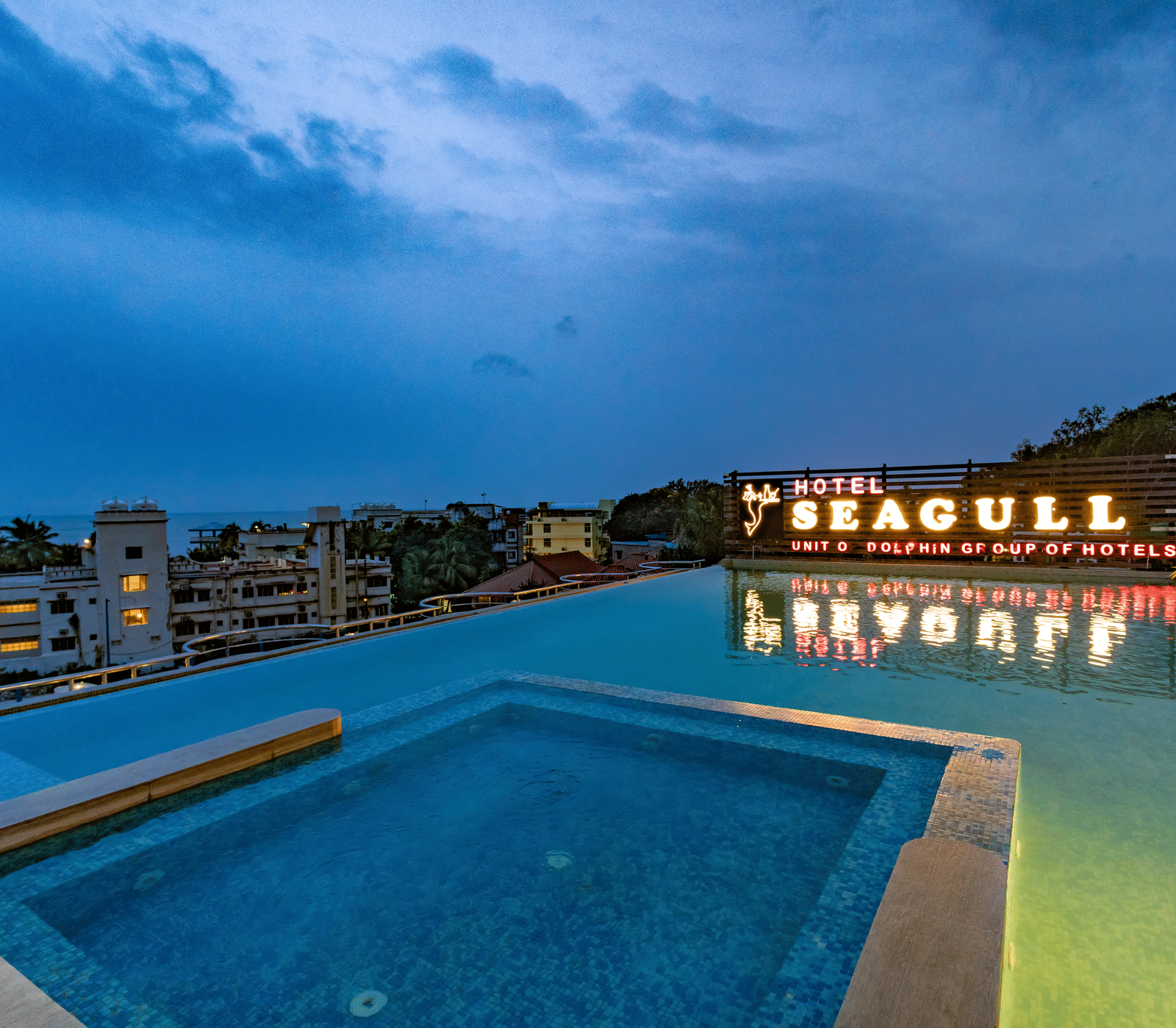 A poolside view with the ‘Seagull’ signage reflected in the swimming pool under a cloudy sky at Hotel Seagull Digha.
