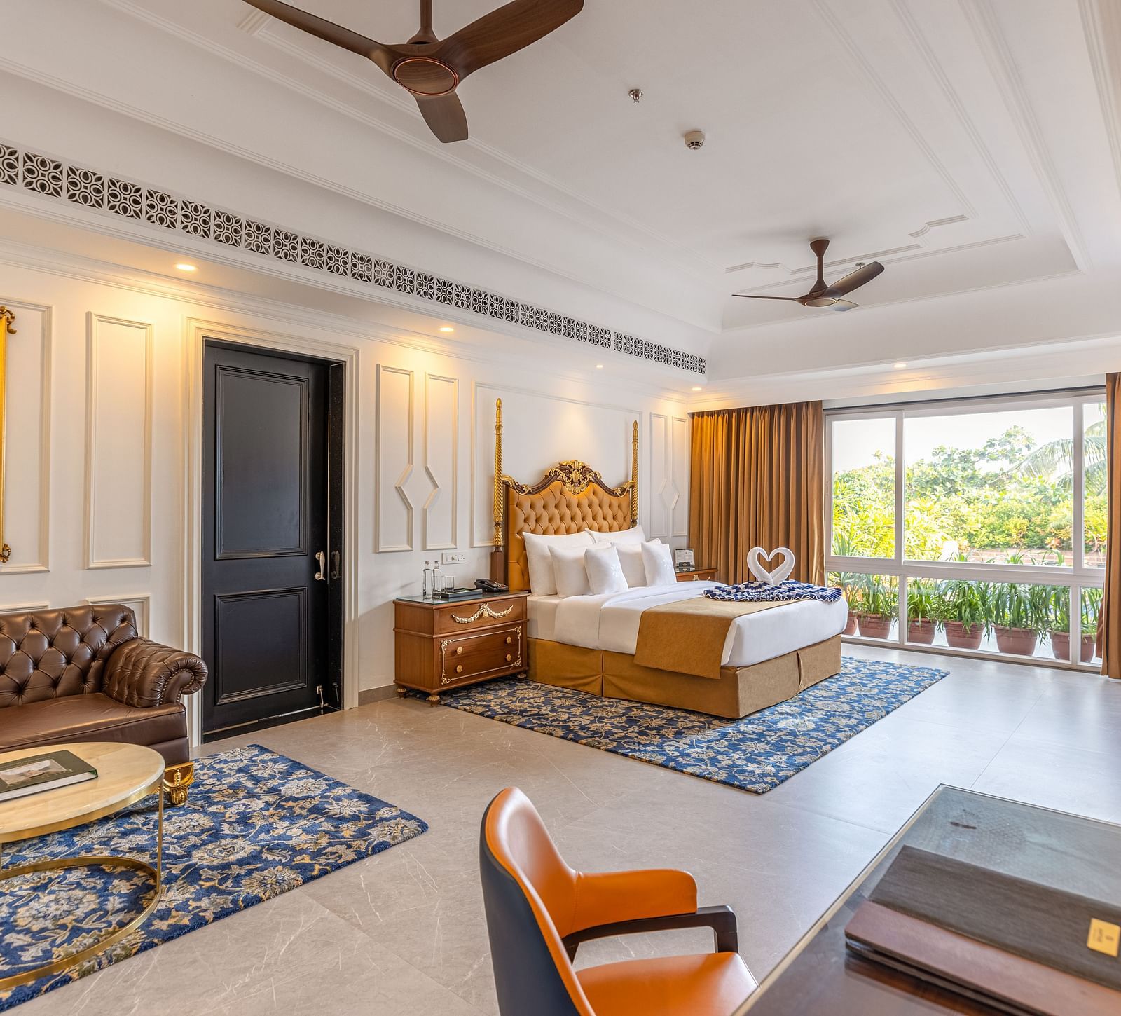 Spacious bedroom with workstation, lounge area, wall-mounted TV, bedside table, two ceiling fans, and large glass windows at MAYFAIR Palm Beach Resort, Gopalpur-On-Sea