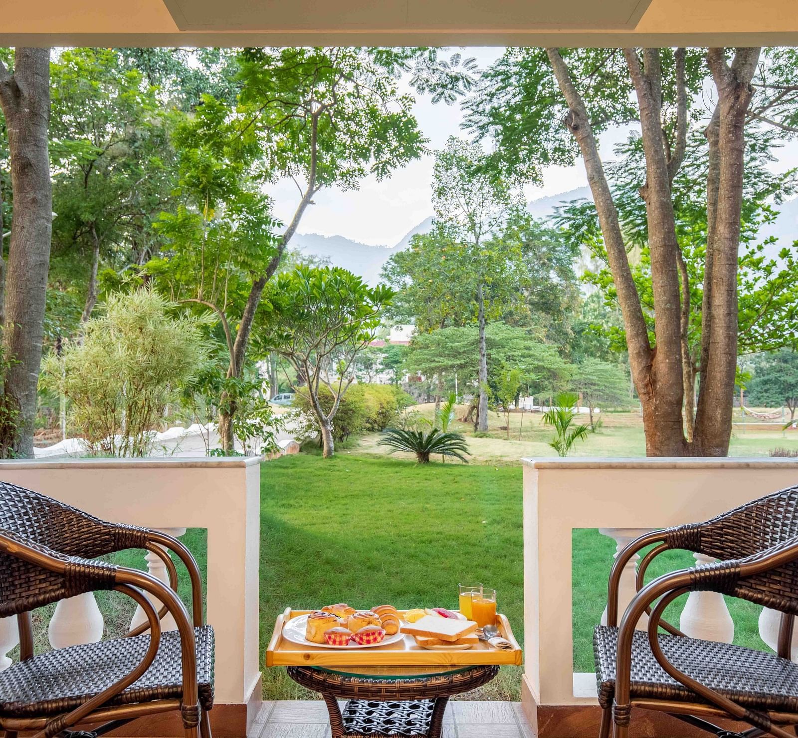 A view from a balcony at Avana Resort overlooking a lush green lawn and numerous trees, with mountains visible in the distance.