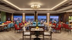 A dining room with a chandelier, blue and red chairs, and tables at Sarovar Portico, Hanumangarh.