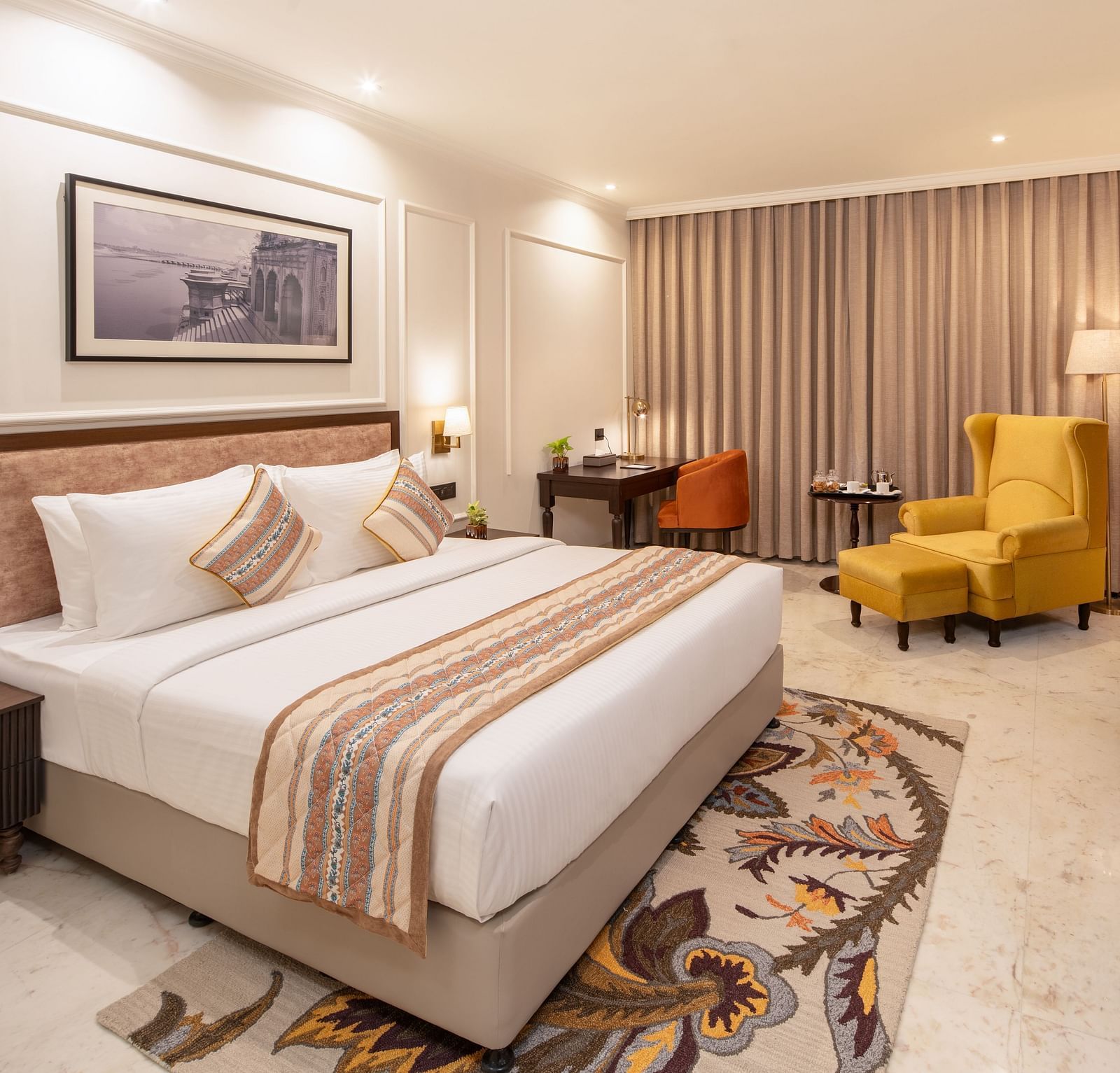 An image of a bedroom with bedside table, photo frame hanged on the wall, work desk with sofa chair, and a flat TV screen - Brij Eternity, Vrindavan
