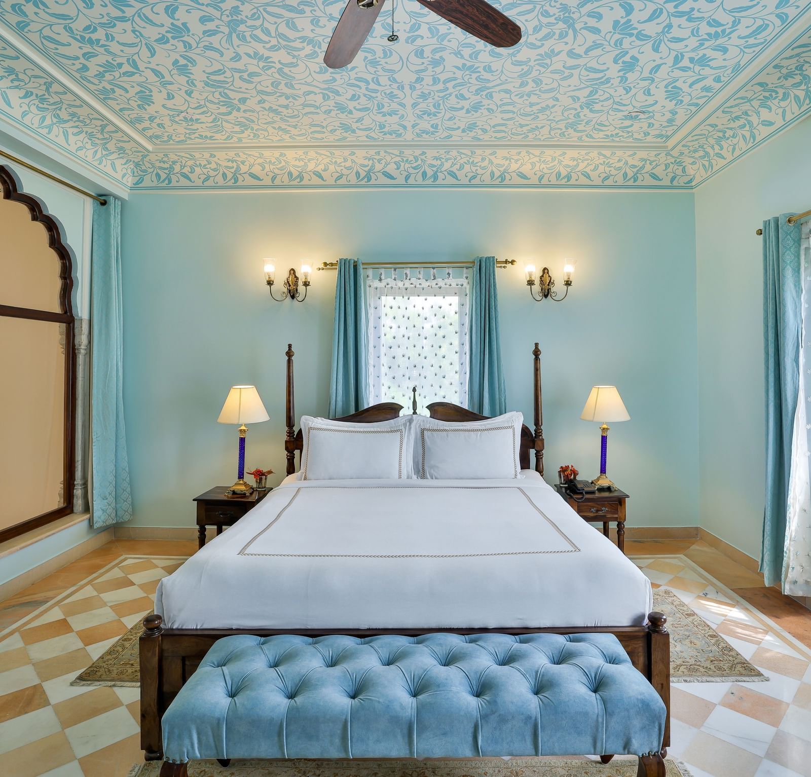 A bedroom at Royal Heritage Haveli with light blue walls, a bed with a white spread, and one arched window