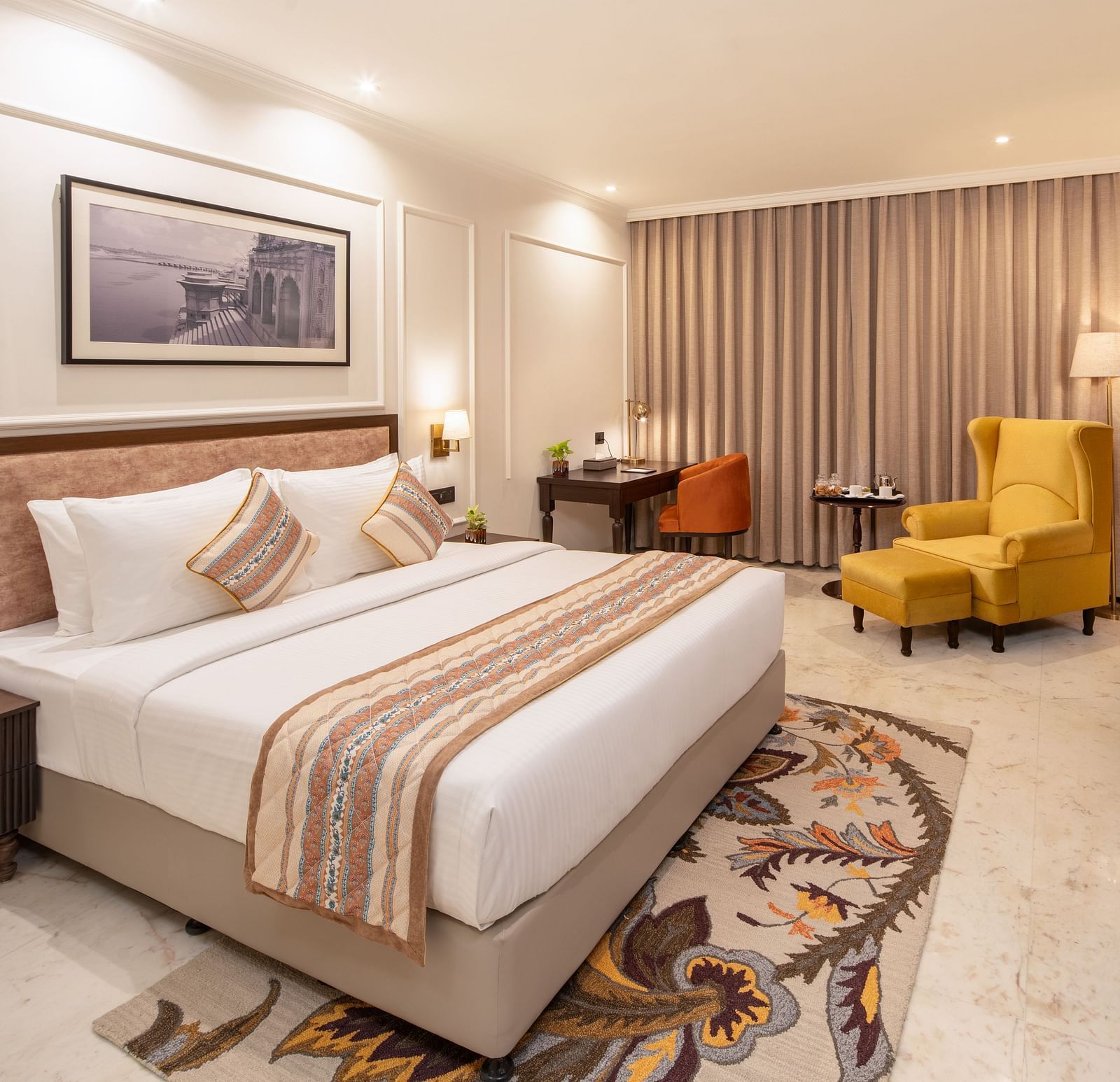 An image of a bedroom with bedside table, photo frame hanged on the wall, work desk with sofa chair, and a flat TV screen - Brij Eternity, Vrindavan