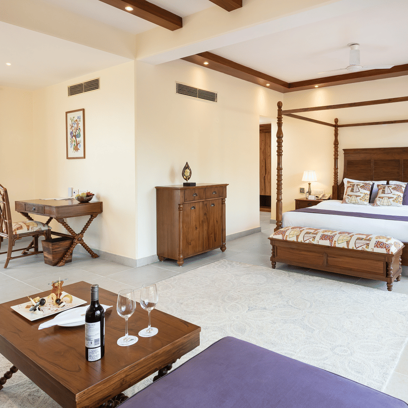 Spacious luxury room with four-poster bed, wooden furniture, seating area, and large windows at Suryavilas Luxury Resort and Spa.