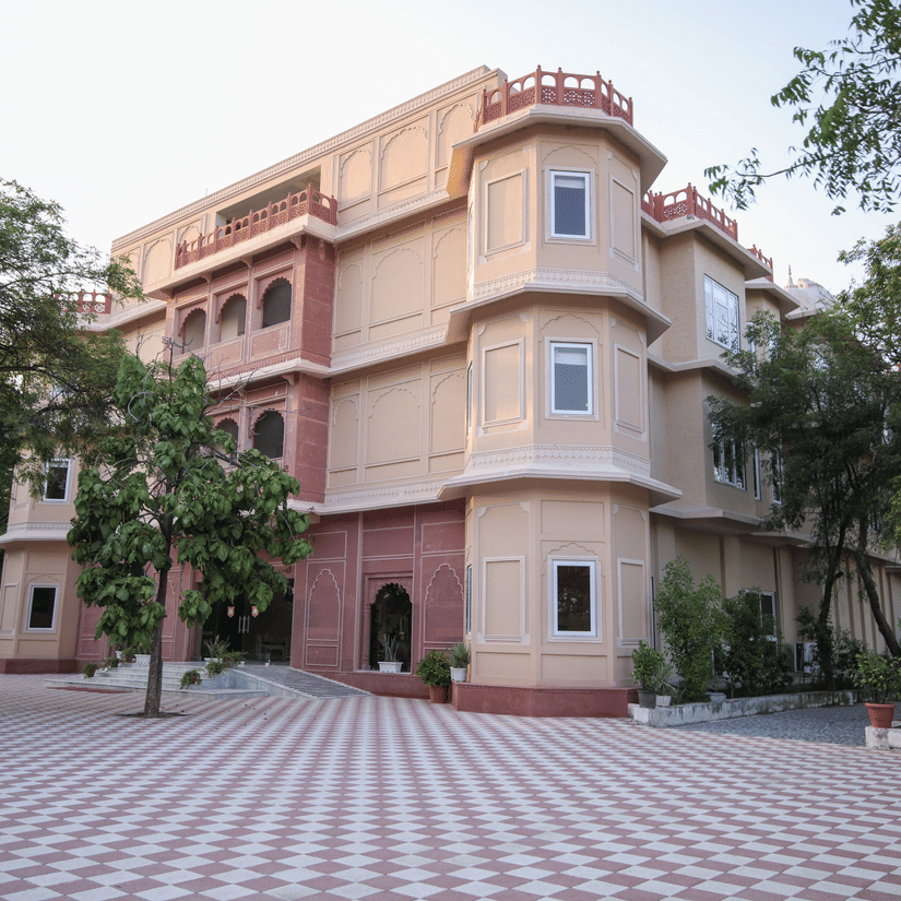 A view of the facade of Ranbanka Ballroom with a large courtyard, trees, and blue sky in the background.