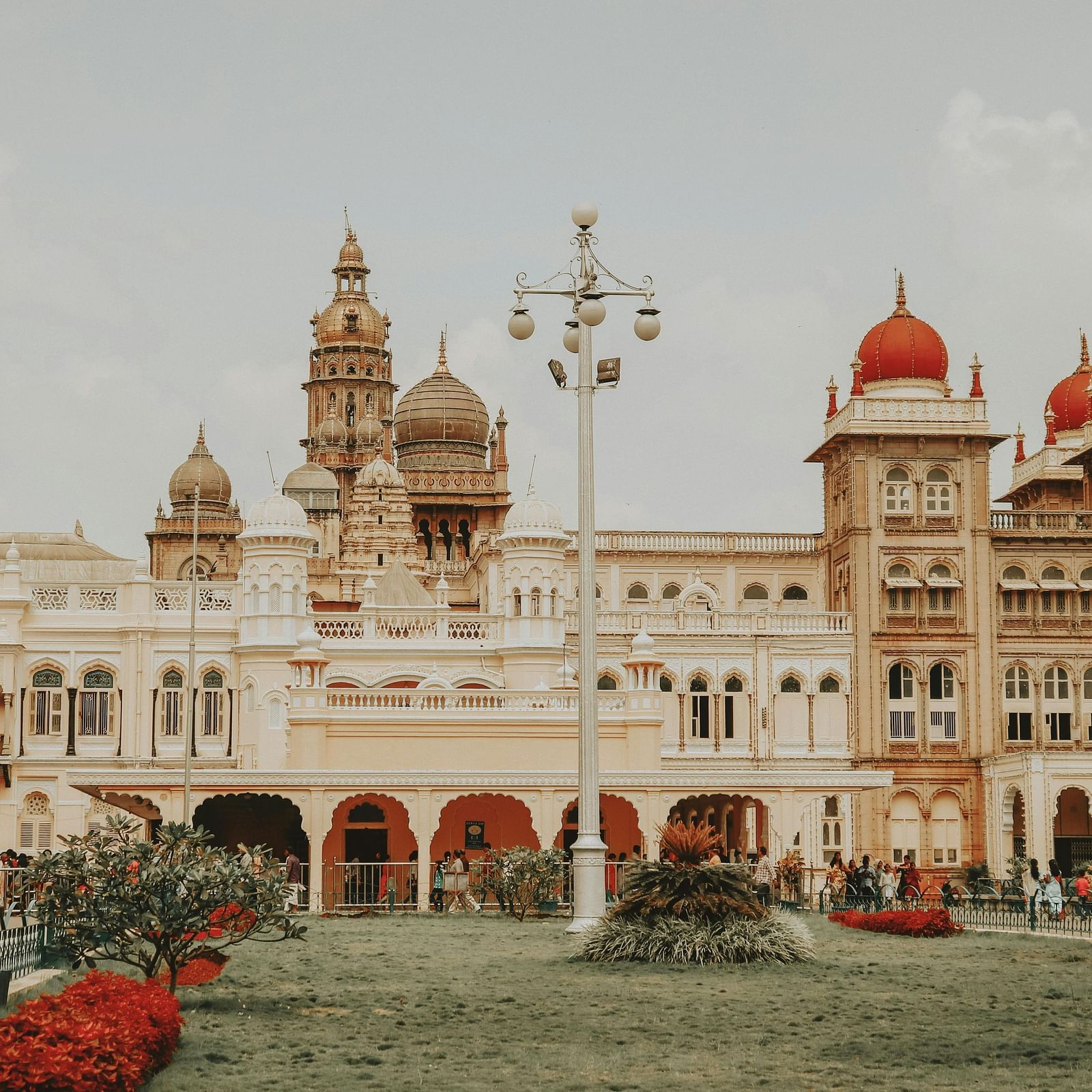 Mysore Palace with ornate architecture, including multiple domes and towers, surrounded by lush gardens and a cloudy sky.