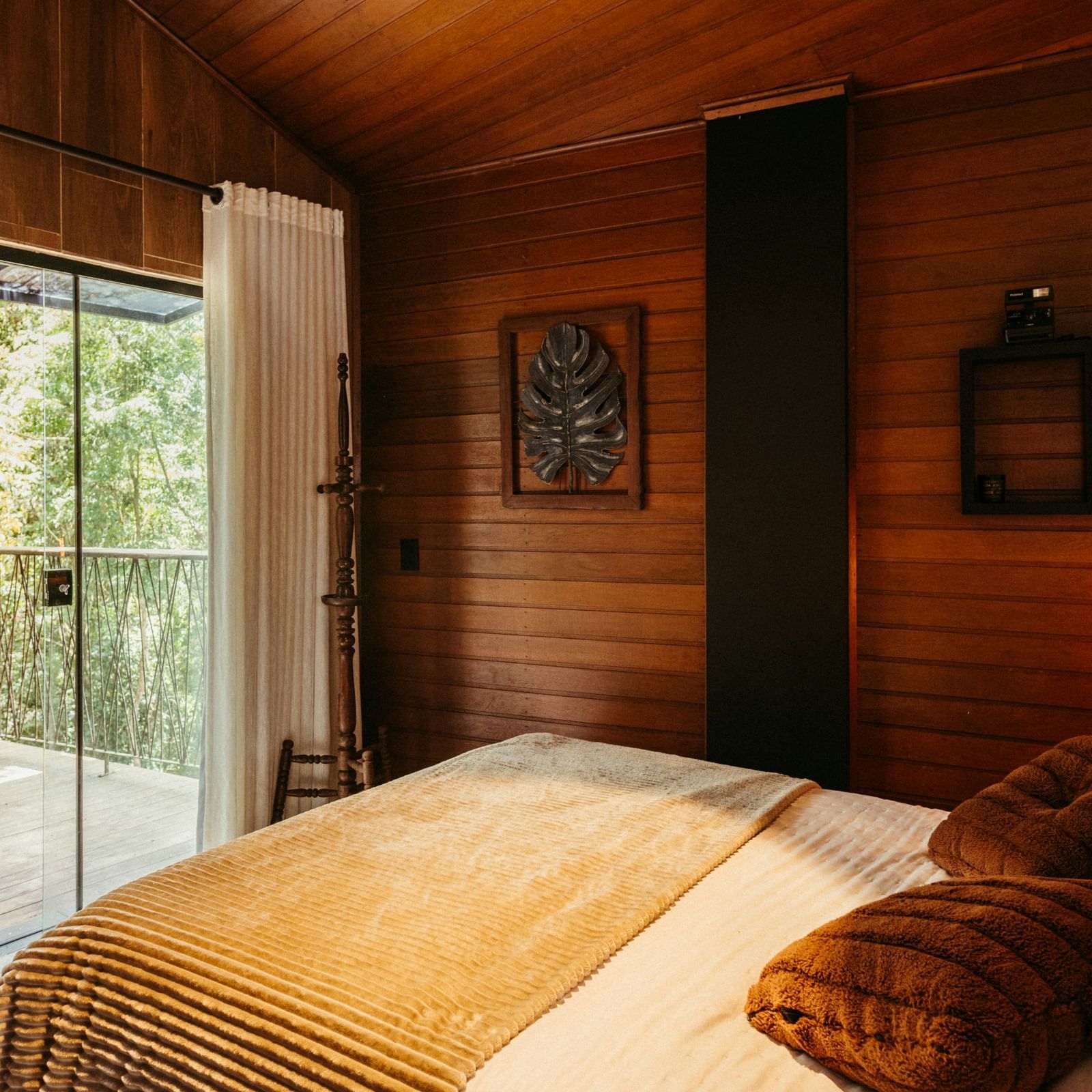 Cabin-style bedroom with wooden walls, cosy lighting, and forest views from the balcony.