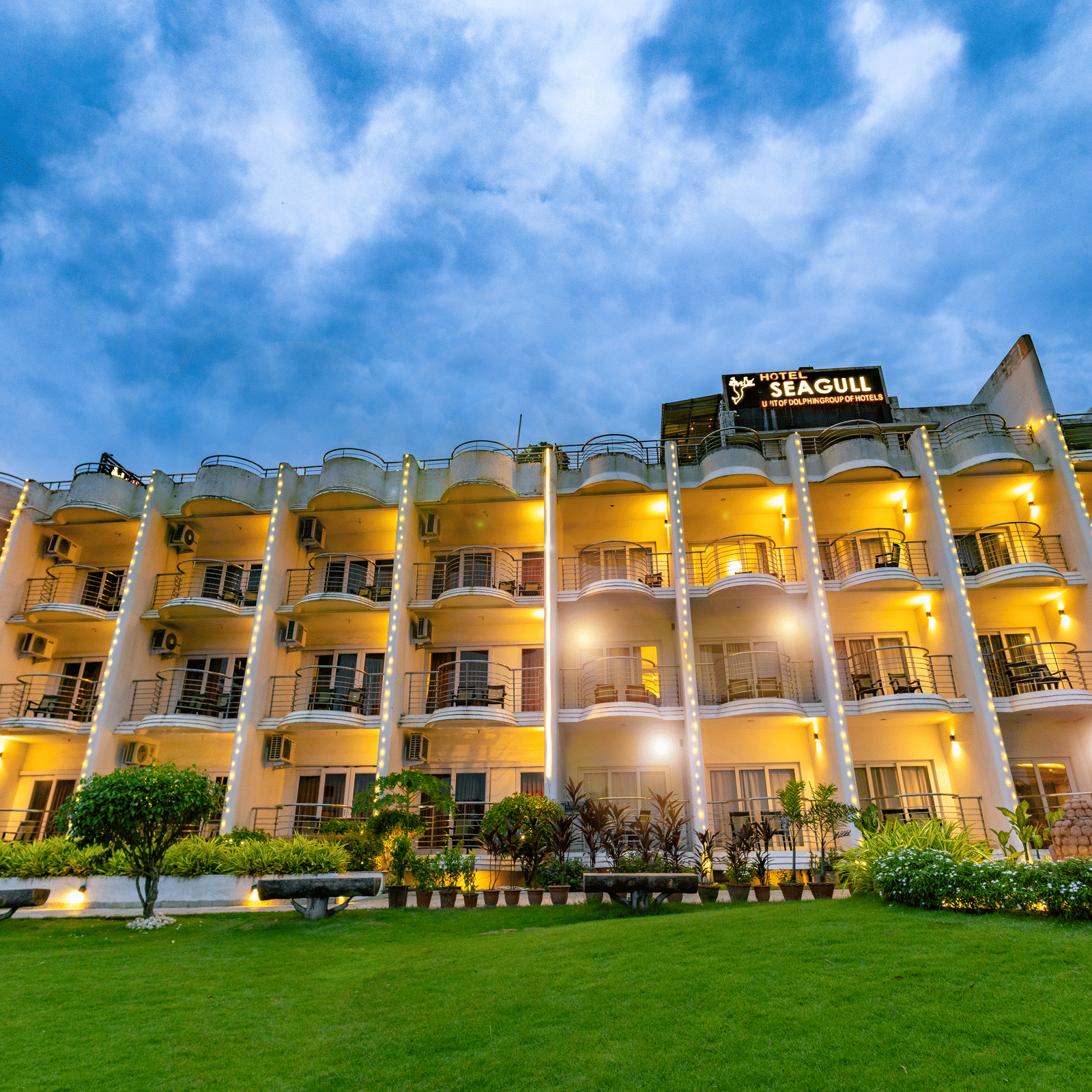 A multi-storey hotel exterior with illuminated windows, and a vibrant green lawn at twilight - Hotel Seagull Digha