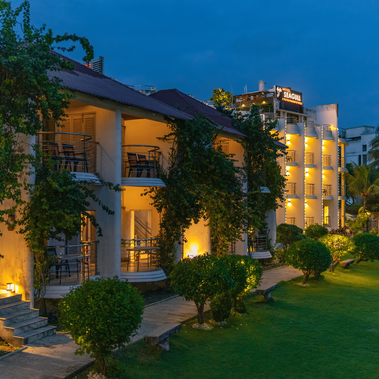 A garden area with pathway, plants, and illuminated building exterior of Hotel Seagull Digha.