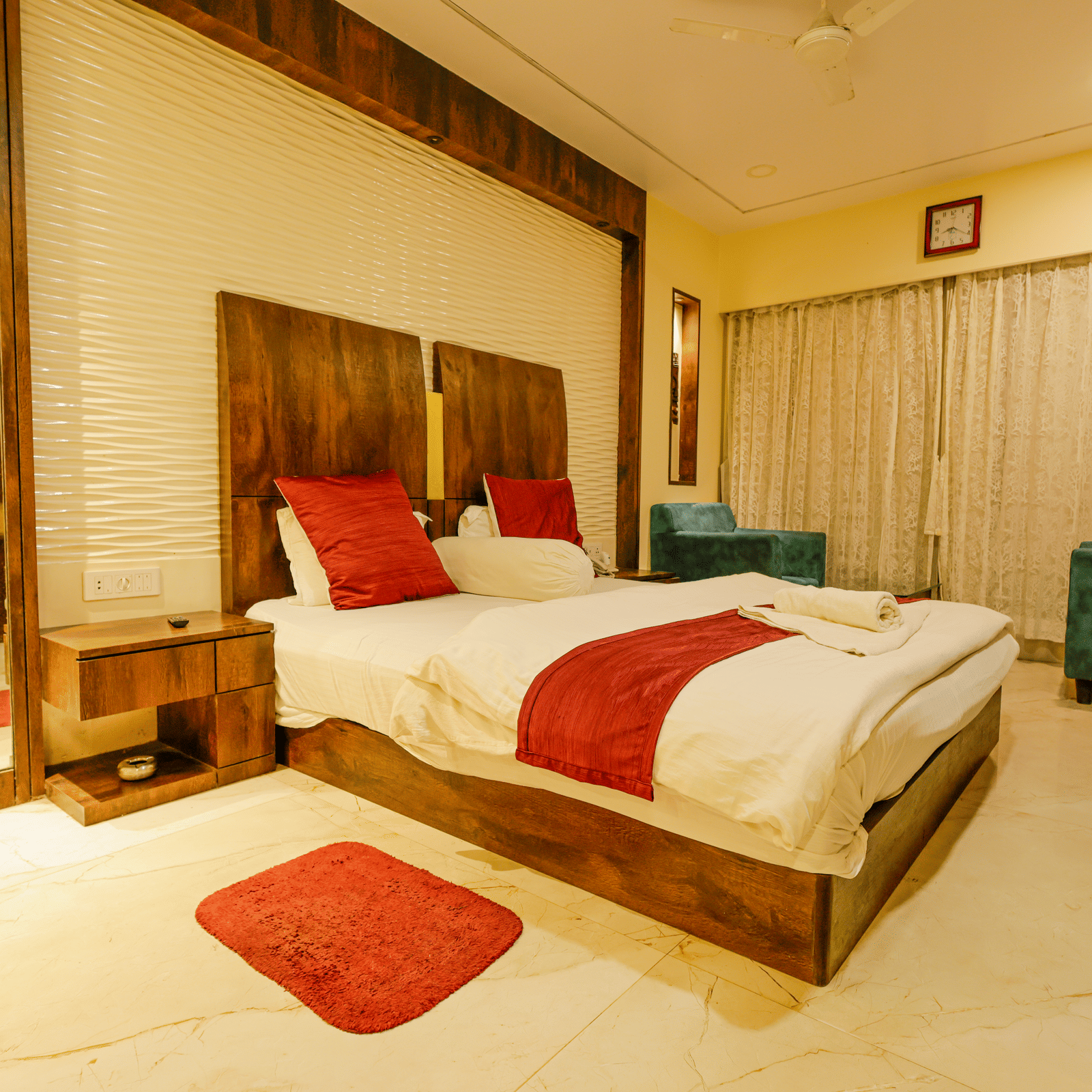A bedroom with a king size bed, red cushions, a mirror, a bedside table and 2 armchairs at Hotel Seagull Digha.