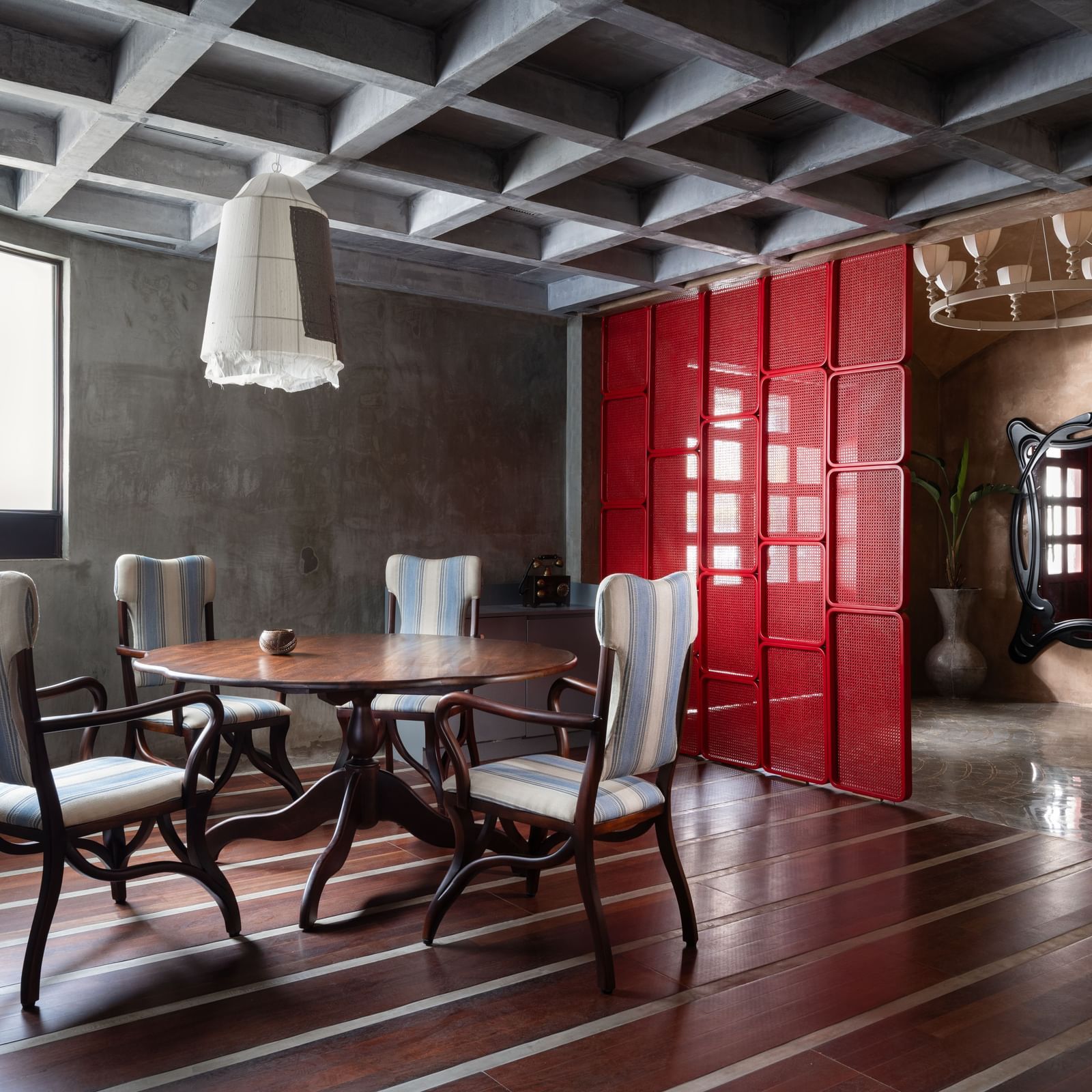 A dining area at Shilton International, Kochi, with a round table, chairs, wooden floor, coffered ceiling, and a partition.