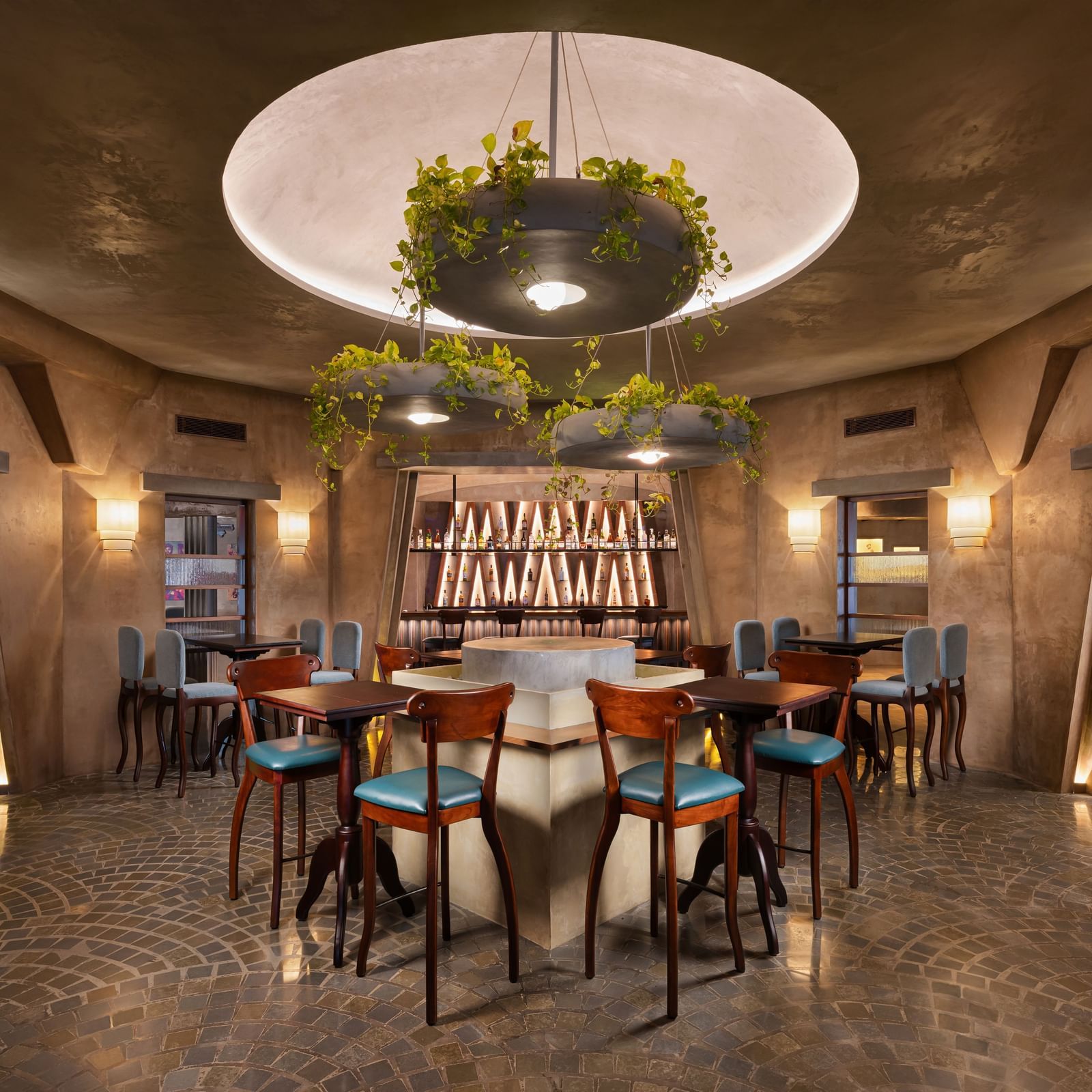 A bar area at Shilton International, Kochi, with a central round bar, stools, and hanging plant decorations.