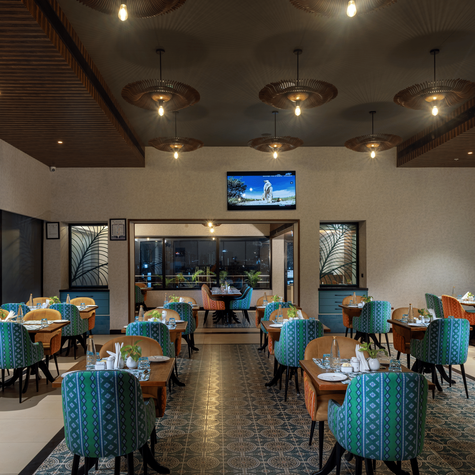 Cosy indoor dining area at Shalimar, the best restaurant in Hyderabad, with patterned flooring, a central TV, and ambient lighting | Zibe Luxe Hyderabad by GRT Hotels