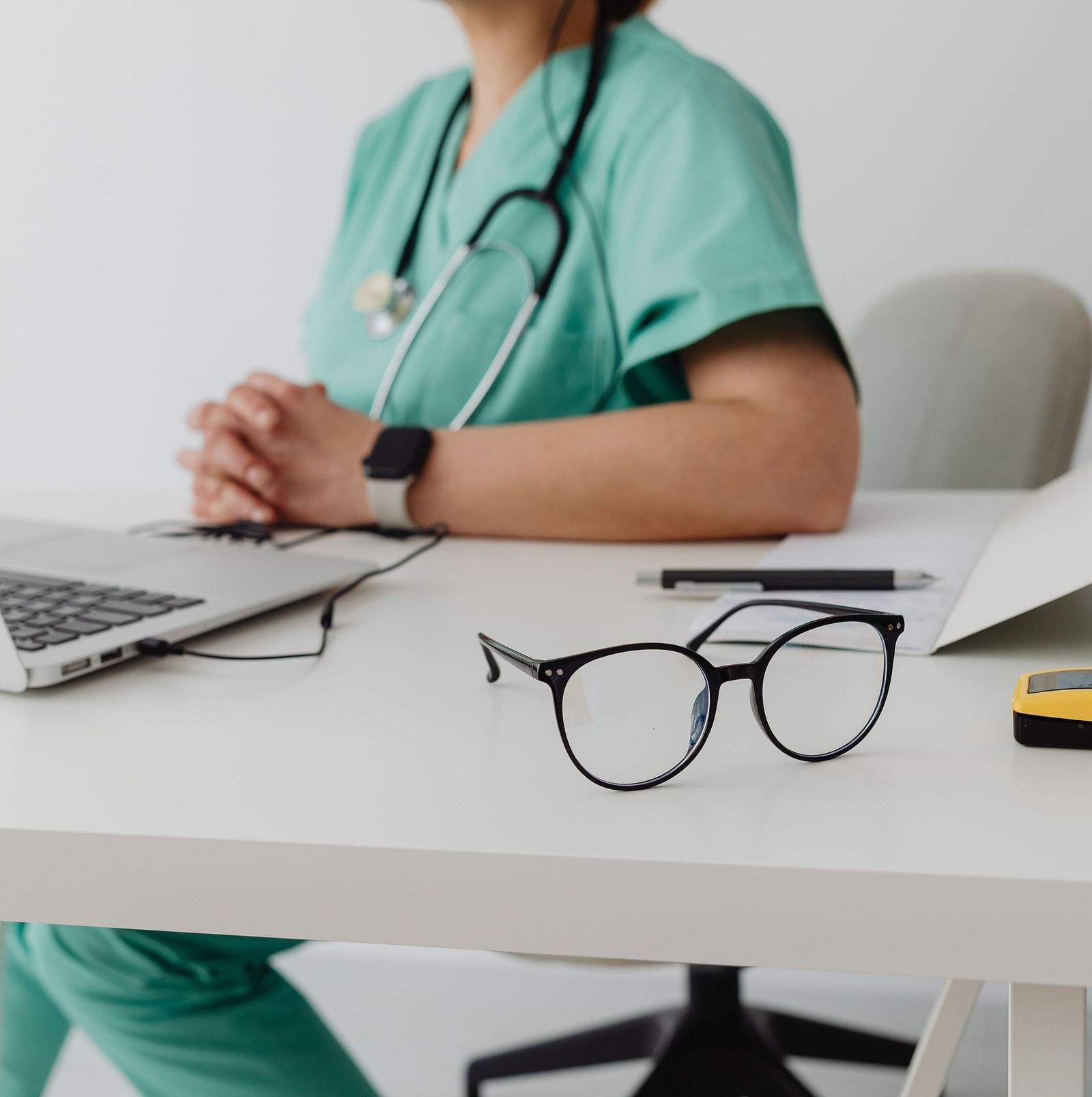 A view of the doctor sitting on chair with laptop open on table.