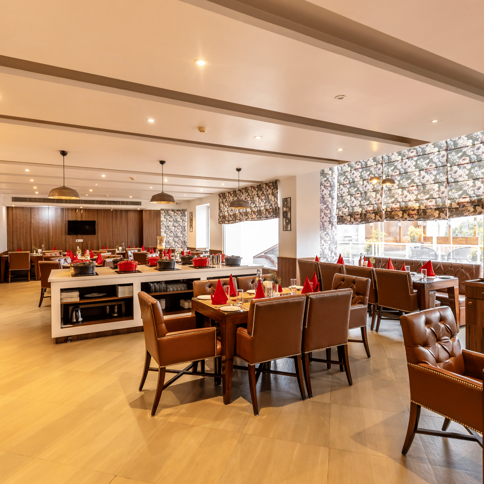 A restaurant with multiple tables, chairs, buffet counters, and lighting fixtures arranged indoors at Indraprastha Resort & Spa, McLeod Ganj.