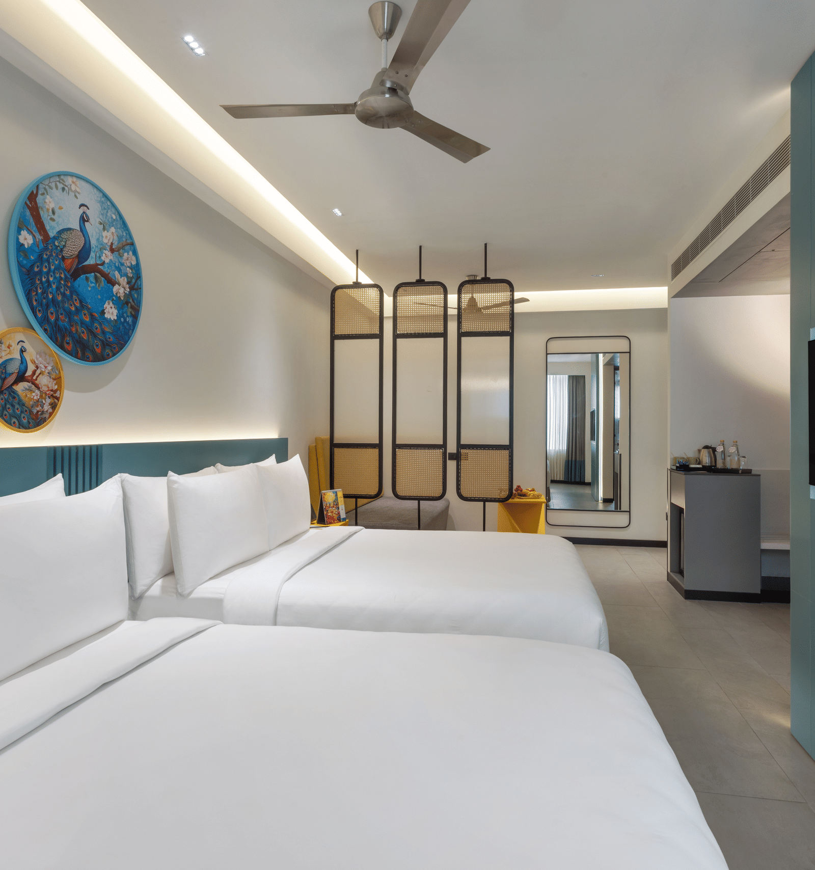 A hotel room with 2 large beds, a wall-mounted TV, a ceiling fan, and a separate seating area making it the best place to stay in Hyderabad for business stays | Zibe Luxe Hyderabad by GRT Hotels