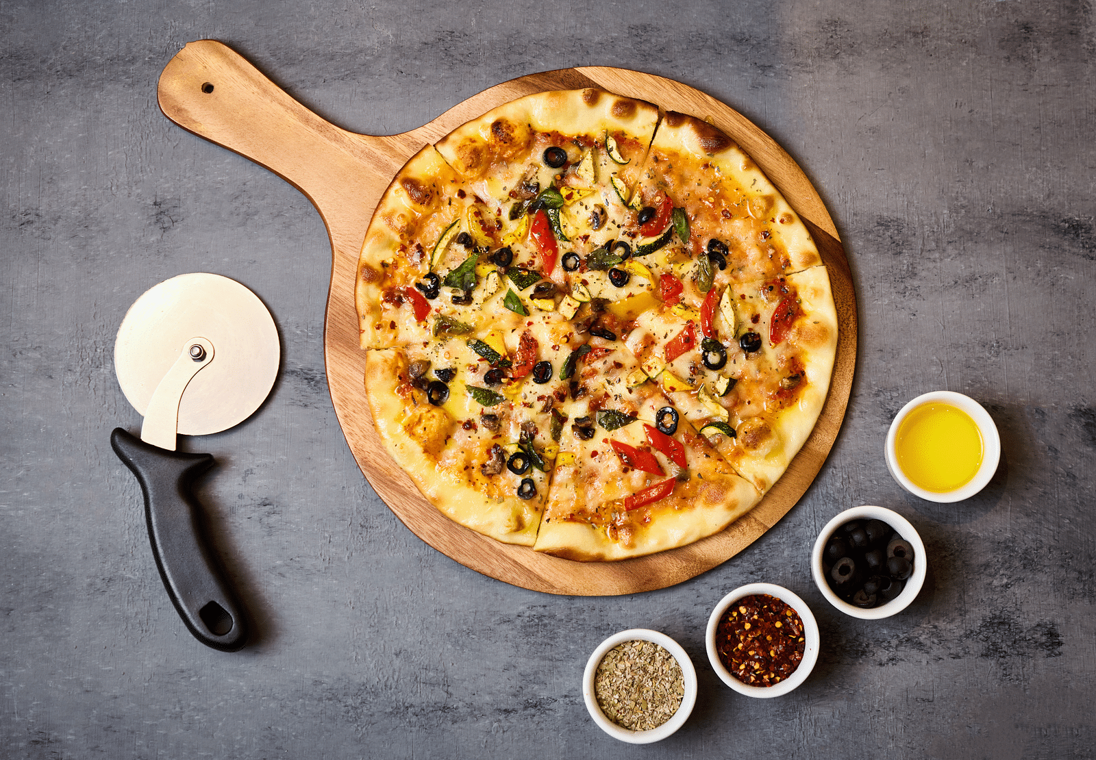 A top angle of a pizza placed on a pan base with sauces placed next to each other.