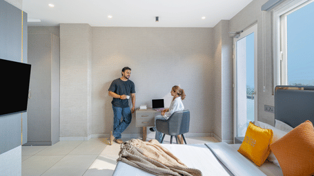 Family with luggage in a bedroom of Lime Tree Hotels & Service Apartment Private Limited featuring a wall mounted television and orange cushions.