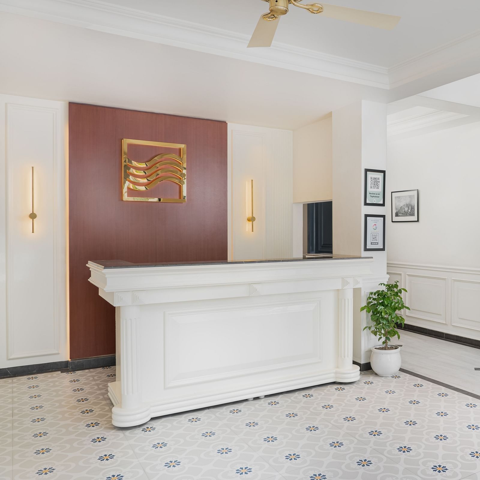 Reception area with a large desk with a potted plant to the side and a staircase on the right | Hotel Ganga Maiya