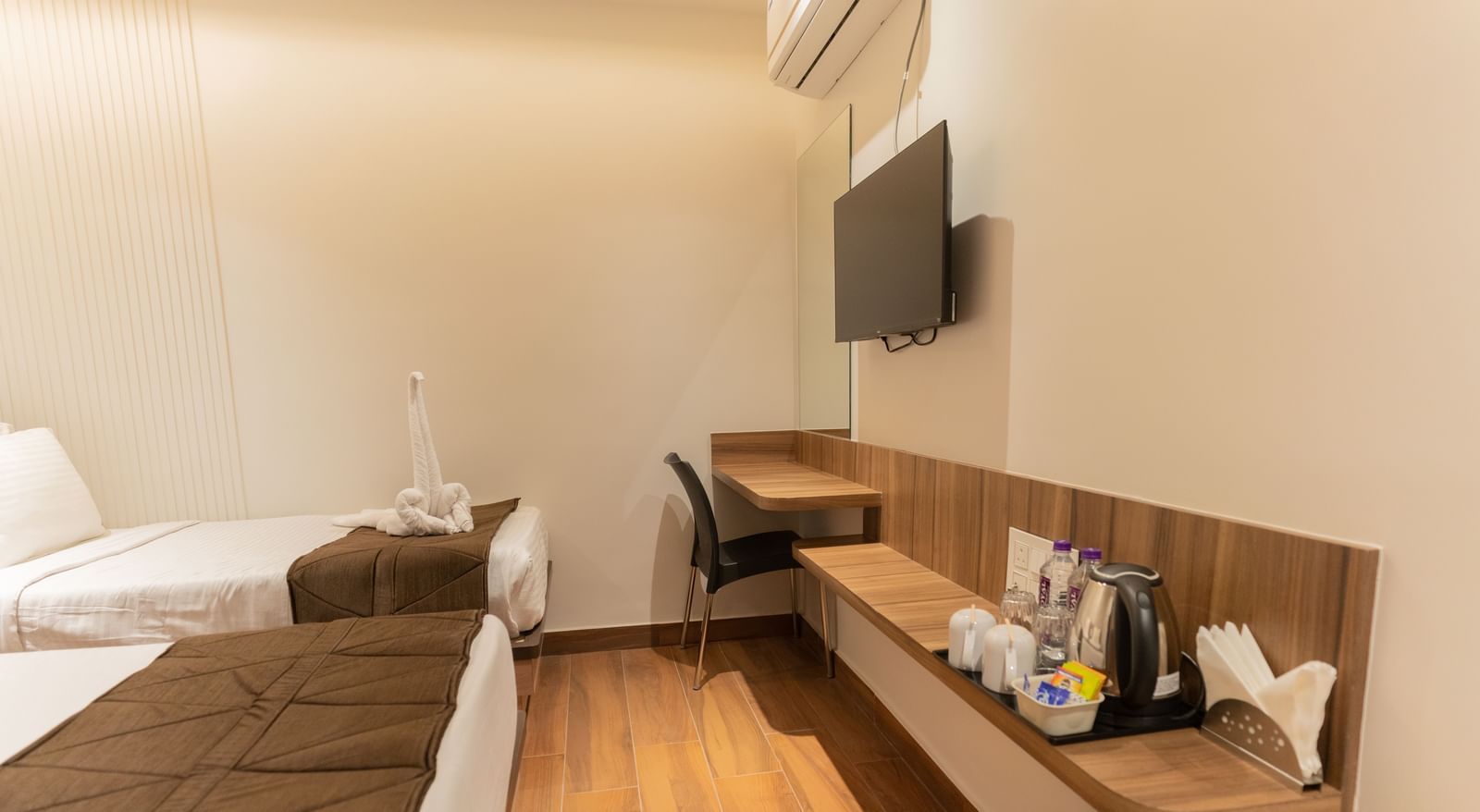 Twin beds with bedside table and wall-mounted TV for convenience at Beestay Hotels, Rajahmundry.