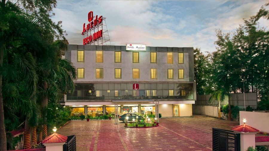 The exterior view of Lords Eco Inn Dahej flanked by green lush vegetation on both its side, featuring red and yellow stone pathway and a circular garden in the foreground.