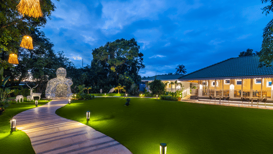 Exterior view of Bonita restaurant in Heritage Village Resort and Spa, Goa featuring a lawn and a pathway.