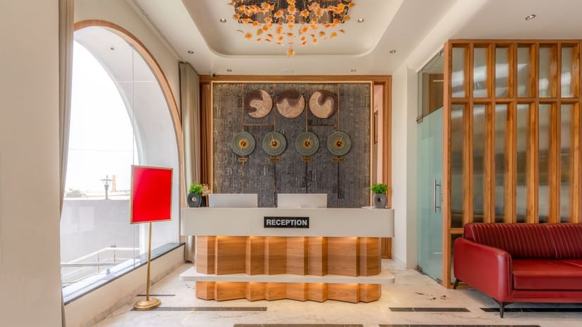Reception desk at Pride Comfort Dwarka which also features clocks of different time zones, a sofa on one side and on the other there is a lamp.
