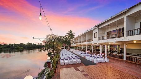 An image of the outdoor event space with seating arrangement near a lake with bright decorative lighting -  GReaT Trails River View Resort Thanjavur By GRT Hotels