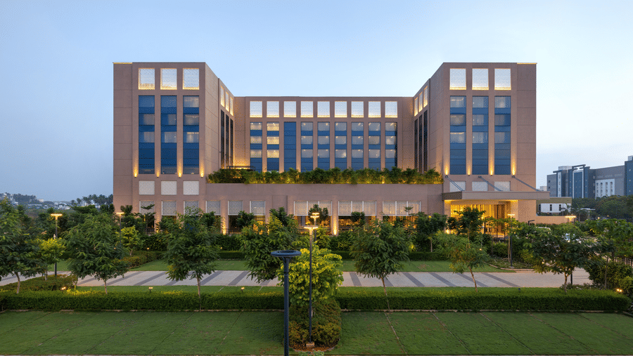 A facade image of our large modern hotel building with numerous windows and manicured landscaping, likely at dusk - Grand Madurai by GRT Hotels