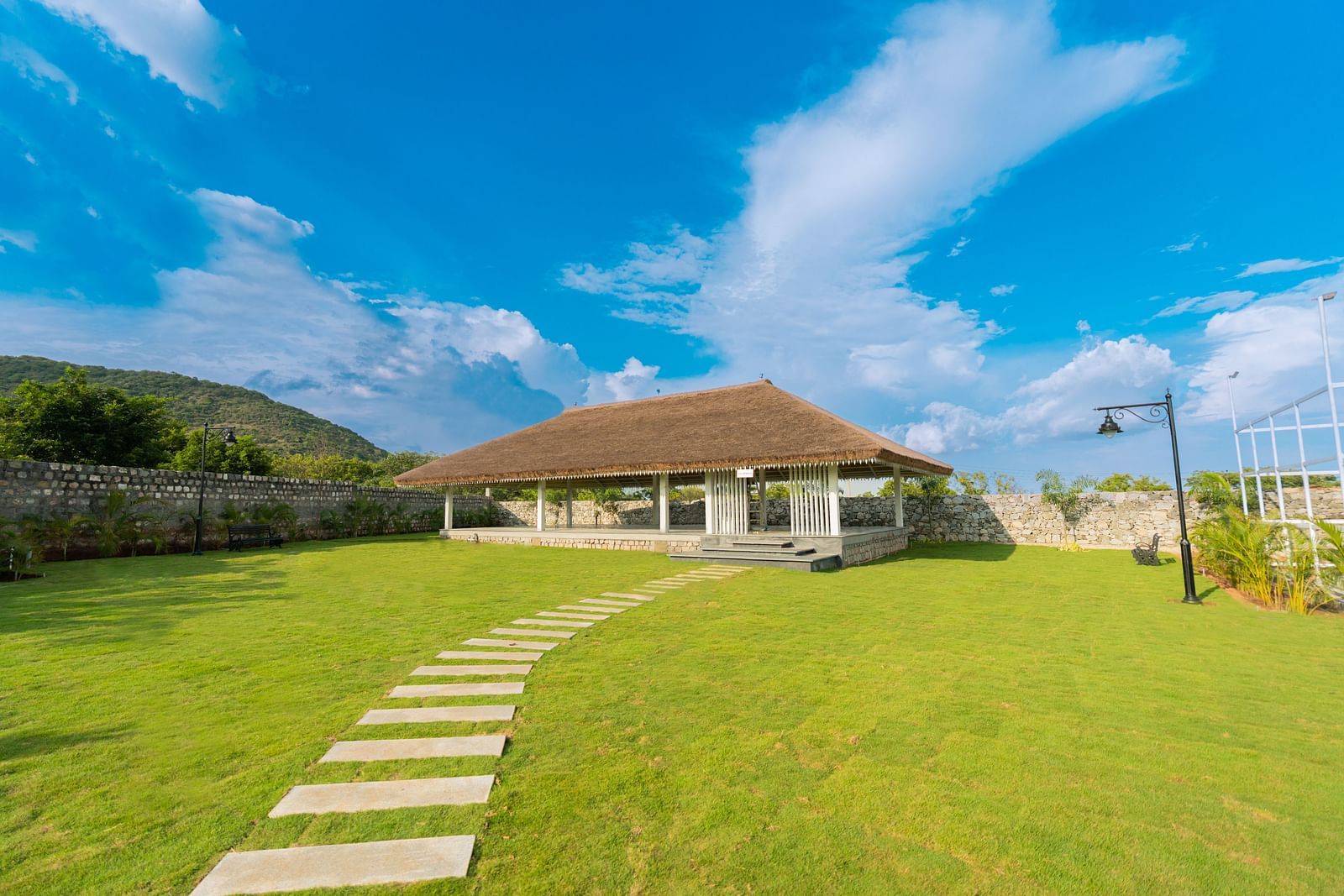 An expansive green lawn with a tile pathway leading towards a sun shade at the slice of heaven - Darza Resorts.