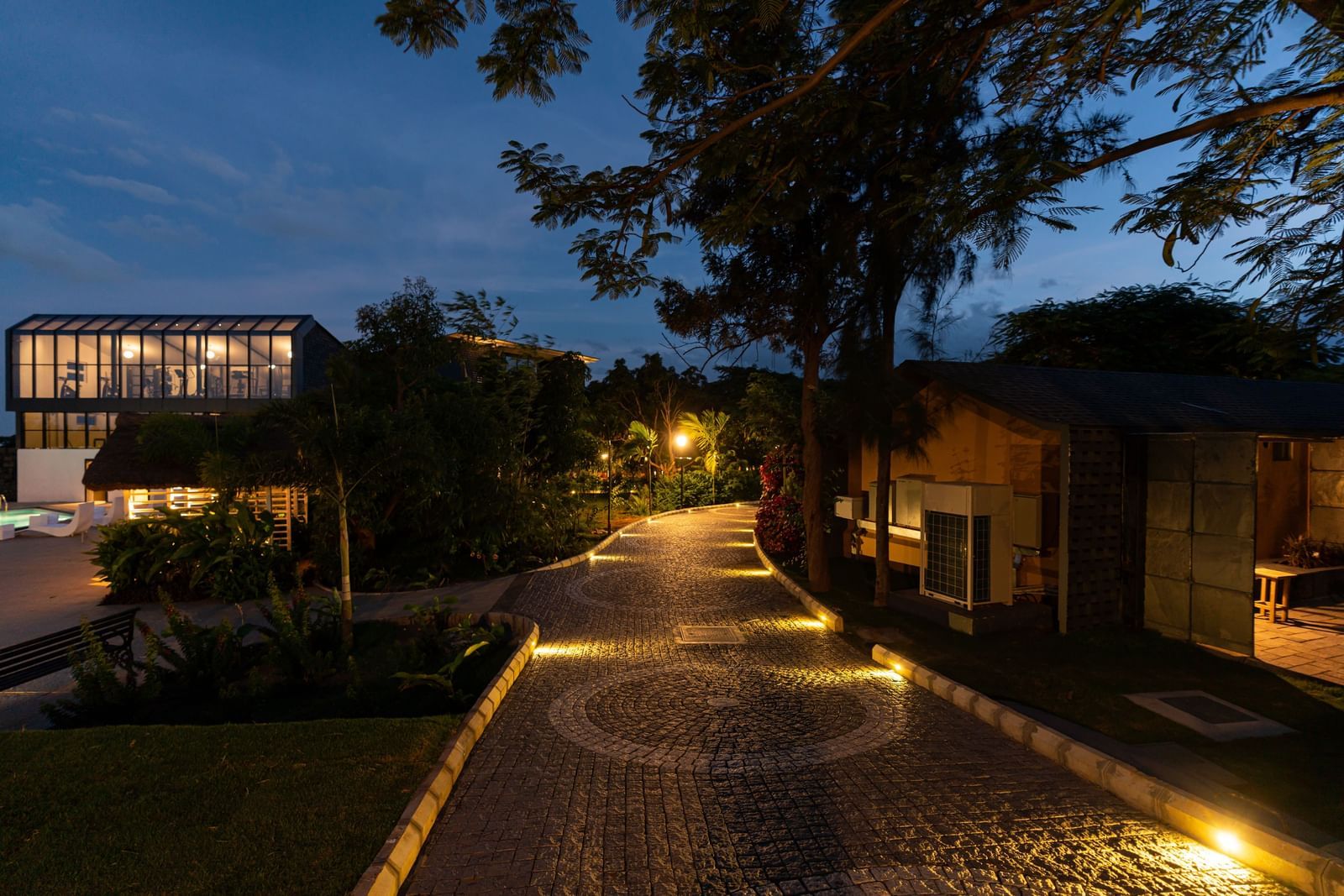 A stone illuminated pathway at Darza Resorts in Coimbatore with trees on both sides and buildings in the background.