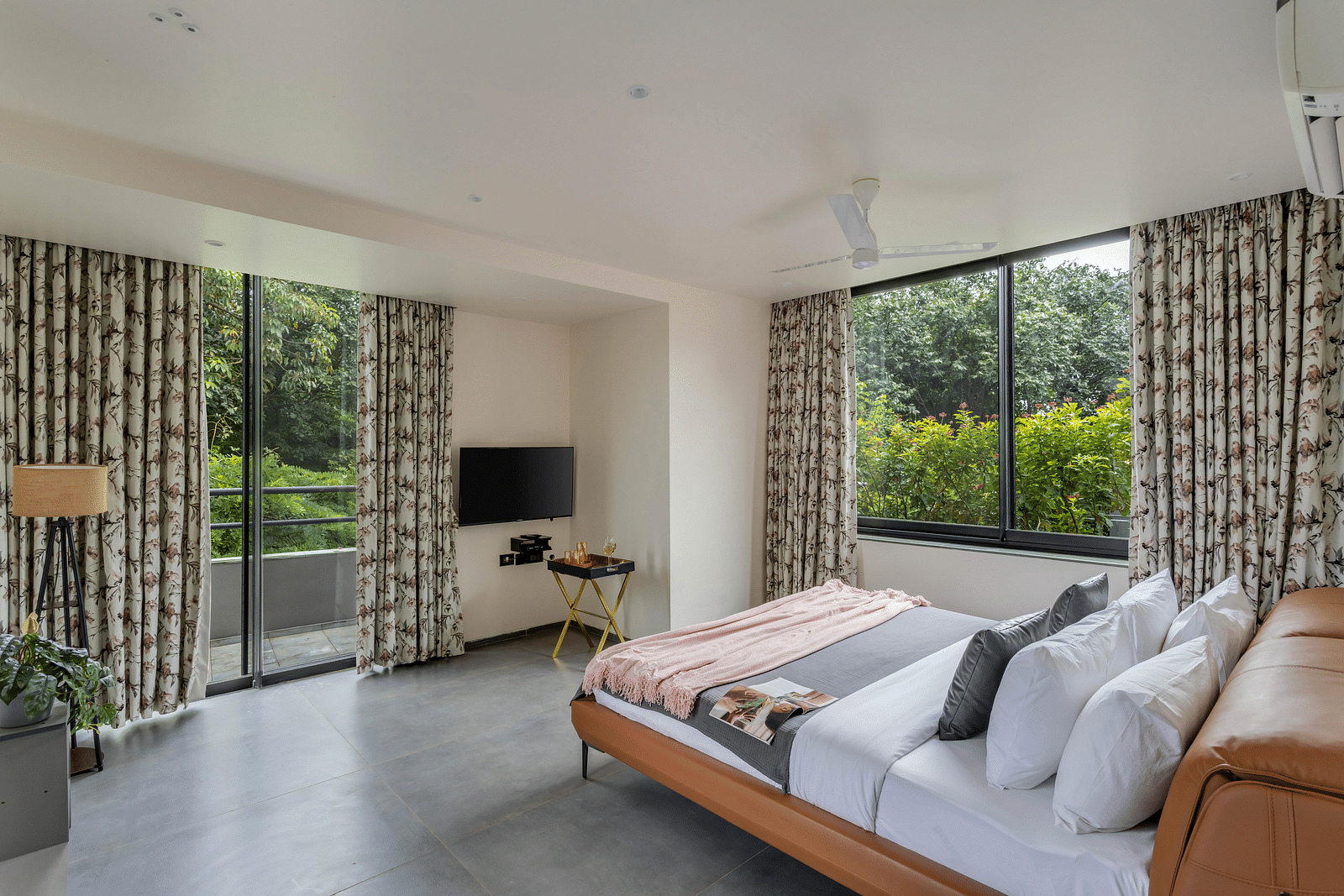 A corner view of a bedroom at Lindsay Manor, featuring a king-size bed, LCD TV, and large windows offering a beautiful view.