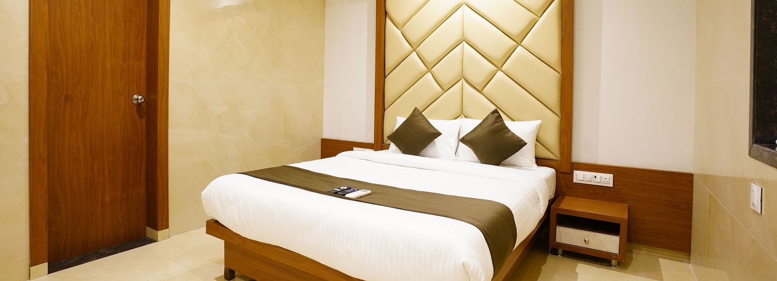Hotel room with a double bed, patterned headboard, and closed door - Shyanu Lords Eco Inn Airoli