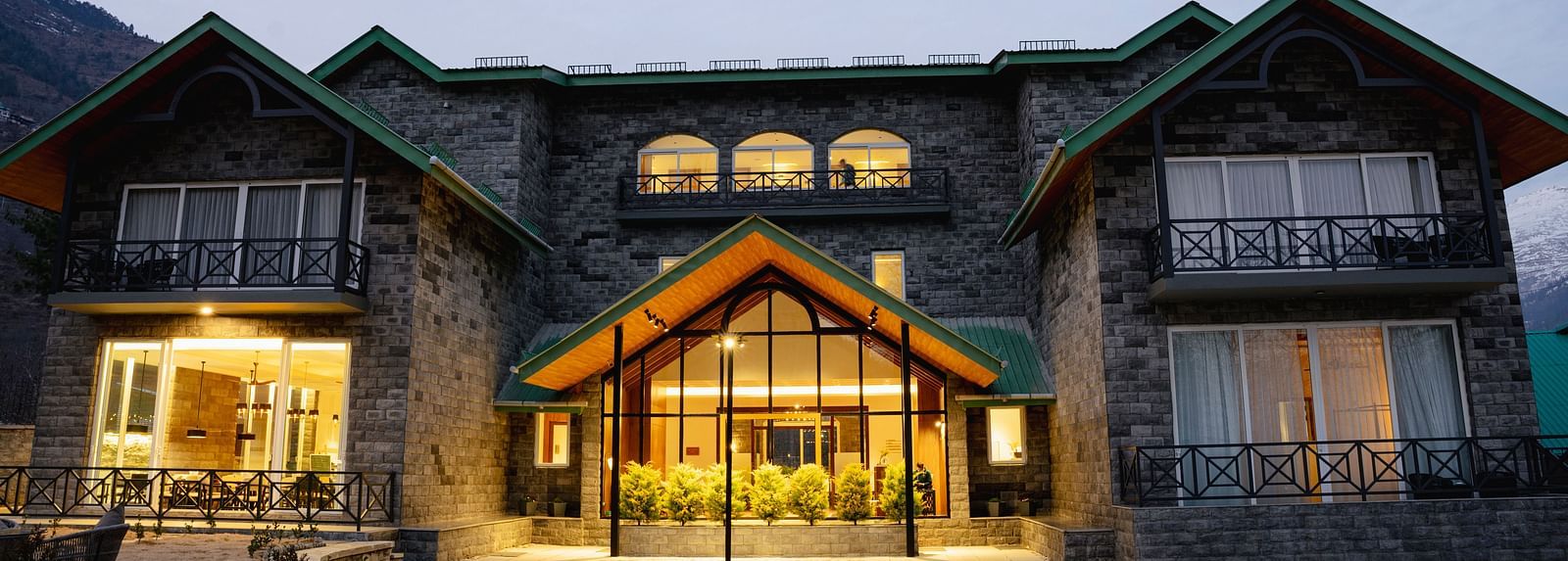 Snow-covered facade with glowing lights at Nivasana Manali during winter dusk.