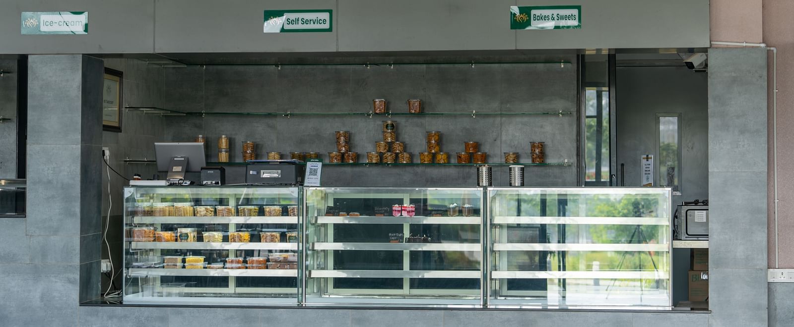 Food counter with snacks placed on glass stands at Hari Govinda's restaurant, with wall-mounted boards above the counter