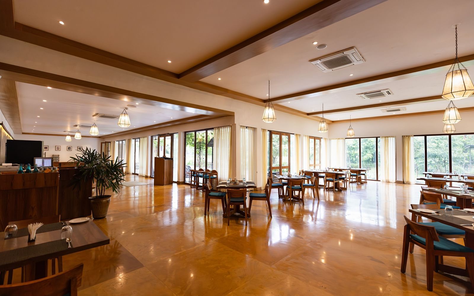 Seating arrangement in Azrak Restaurant at Saraca Resort & Spa Corbett with wooden flooring and wooden panelling on the ceiling alongside large French windows bringing in lots of light
