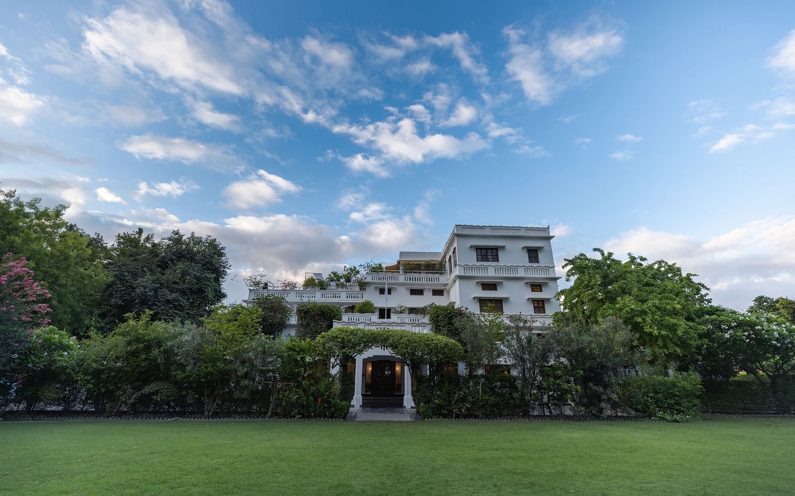 A wide view of the garden area of Saraca Hotel, Lucknow with the hotel building in the background on a cloudy day