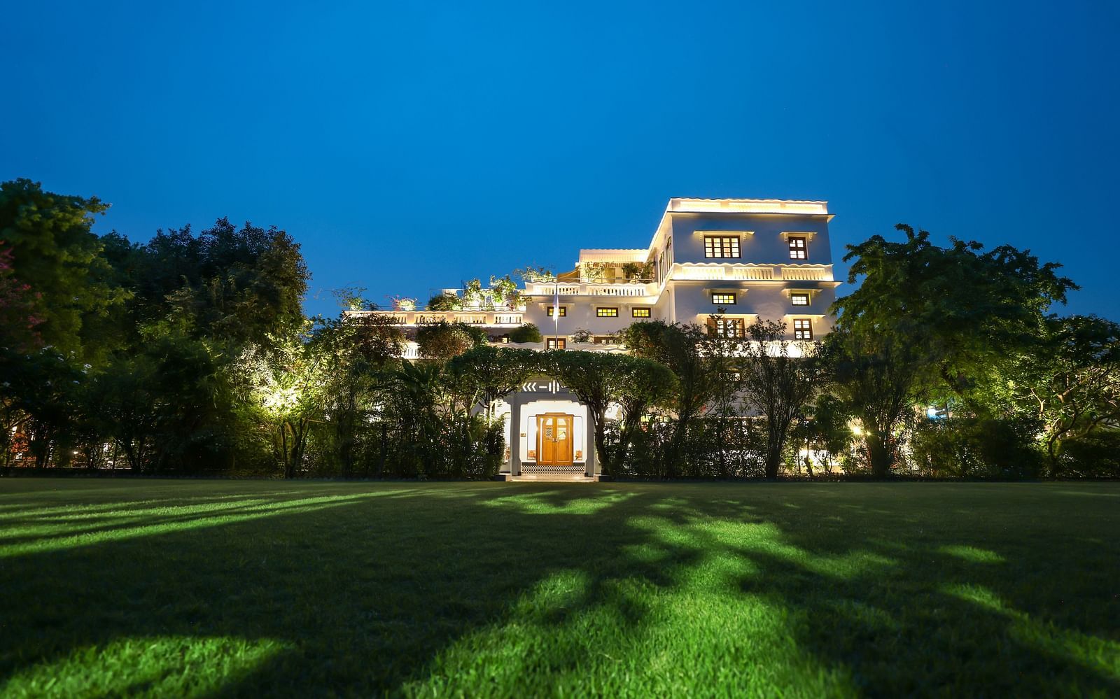 A wide view of the garden area of Saraca Hotel, Lucknow with the hotel building in the background during blue hour
