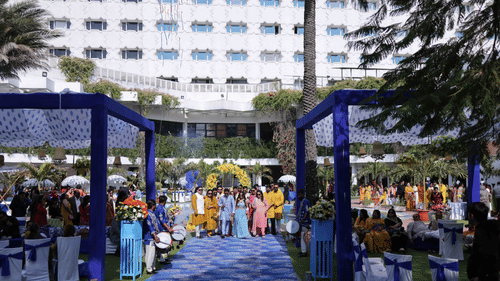 Guests walking through a beautifully decorated outdoor wedding venue featuring floral arrangements, ceremonial drummers, elegant seating, and vibrant event decor at Clarks Amer, Jaipur.