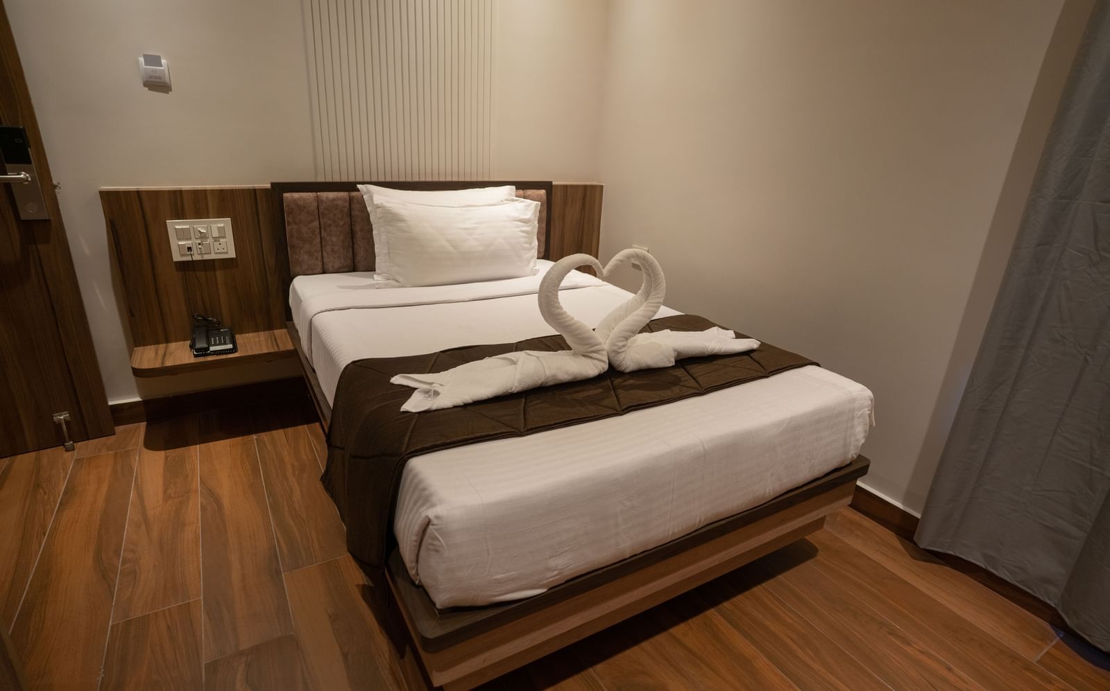 Neatly arranged single bed with towel swan decoration and bedside table at Beestay Hotels, Rajahmundry.