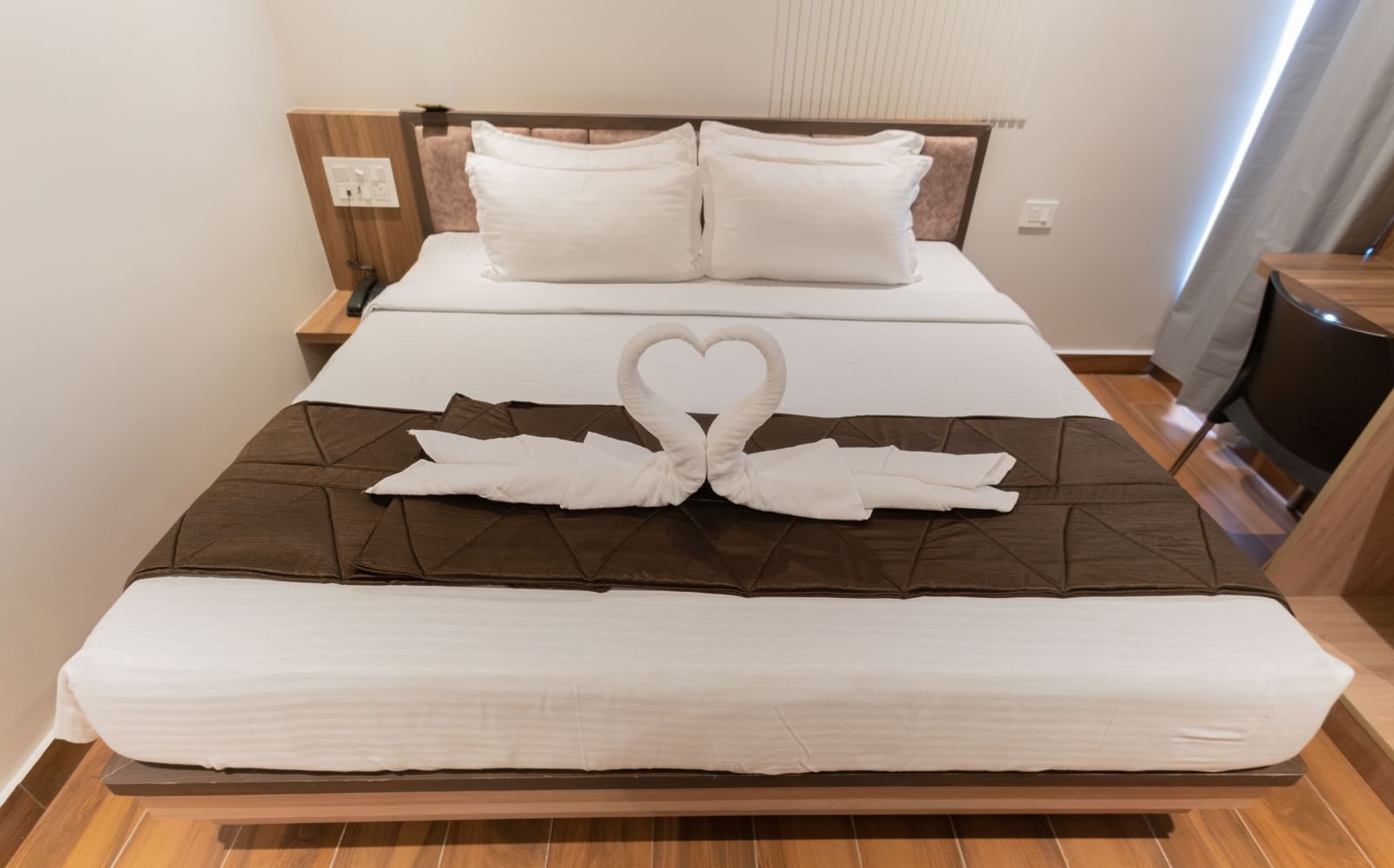 View of a spacious bed with neatly arranged swan decorations made from towels at Beestay Hotels, Rajahmundry.