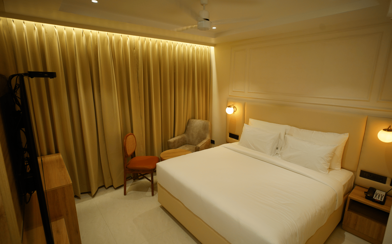Elegant double room at Monday Premium, Madhapur, featuring a large bed, gold curtains, and a seating area with a small table.