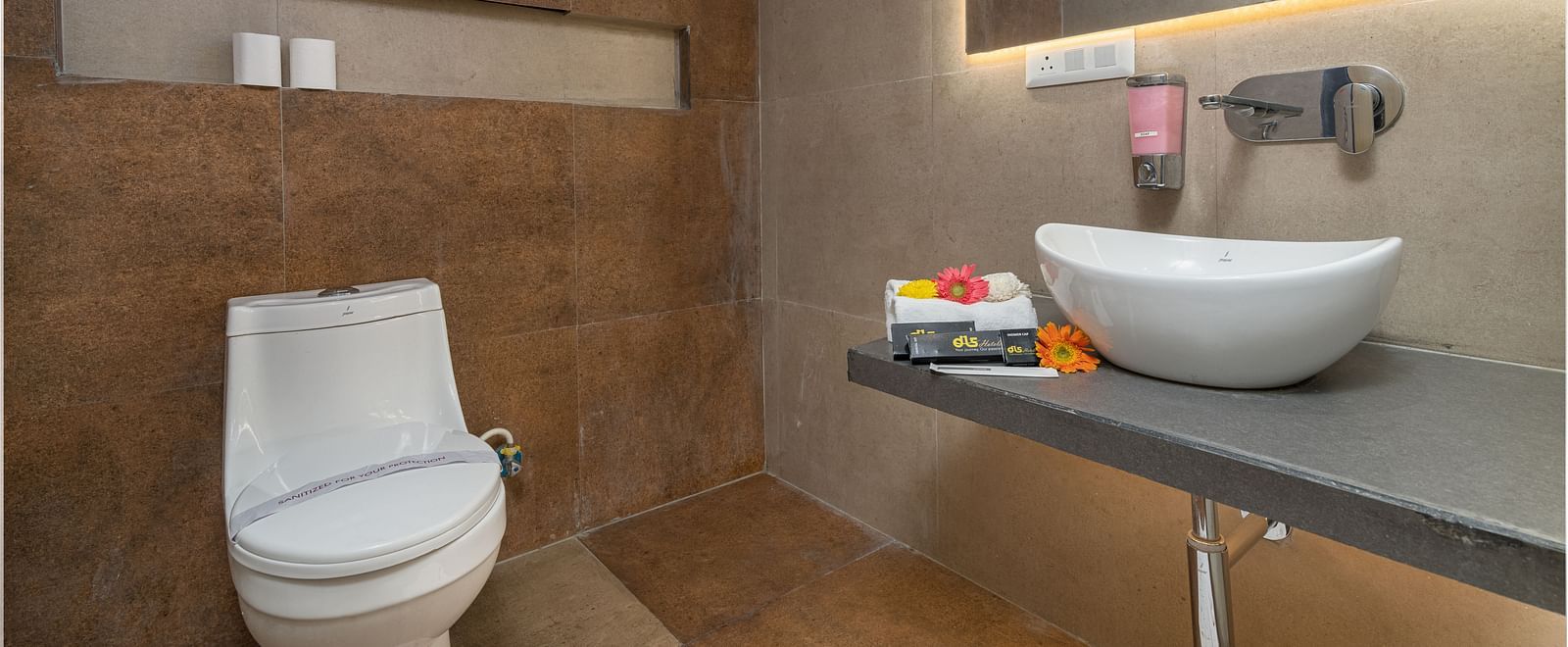 An image of a washroom in the deluxe room showcasing the toilet seat, wash area and wall mounted mirror - DLS Ganga Bliss, Haridwar