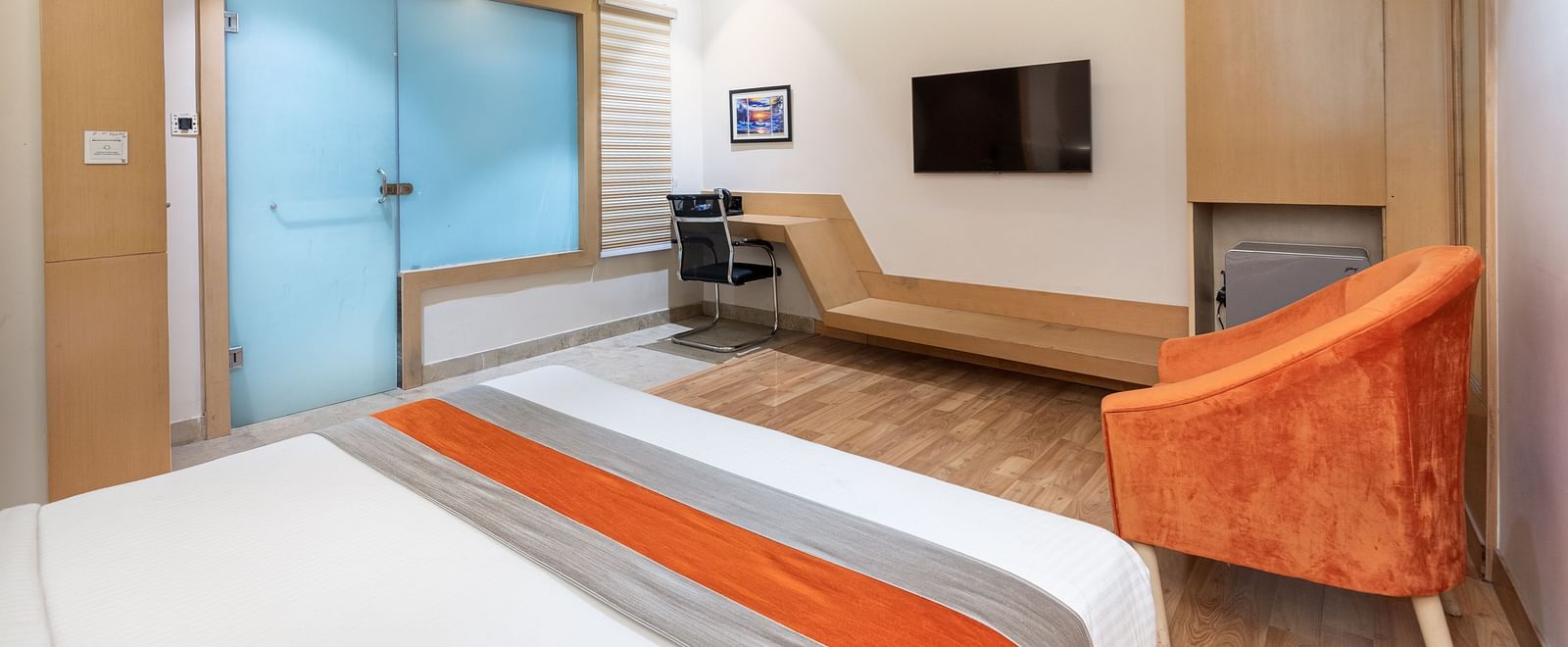 An image of the deluxe room at DLS Hotel Arihant, Haridwar with a bed, a chair, and a flat screen TV