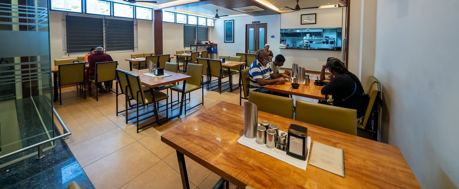 Diagonal view of the dining area at Hari Govinda's, with a neatly arranged table and chairs, and lighting featured in the ceiling corner