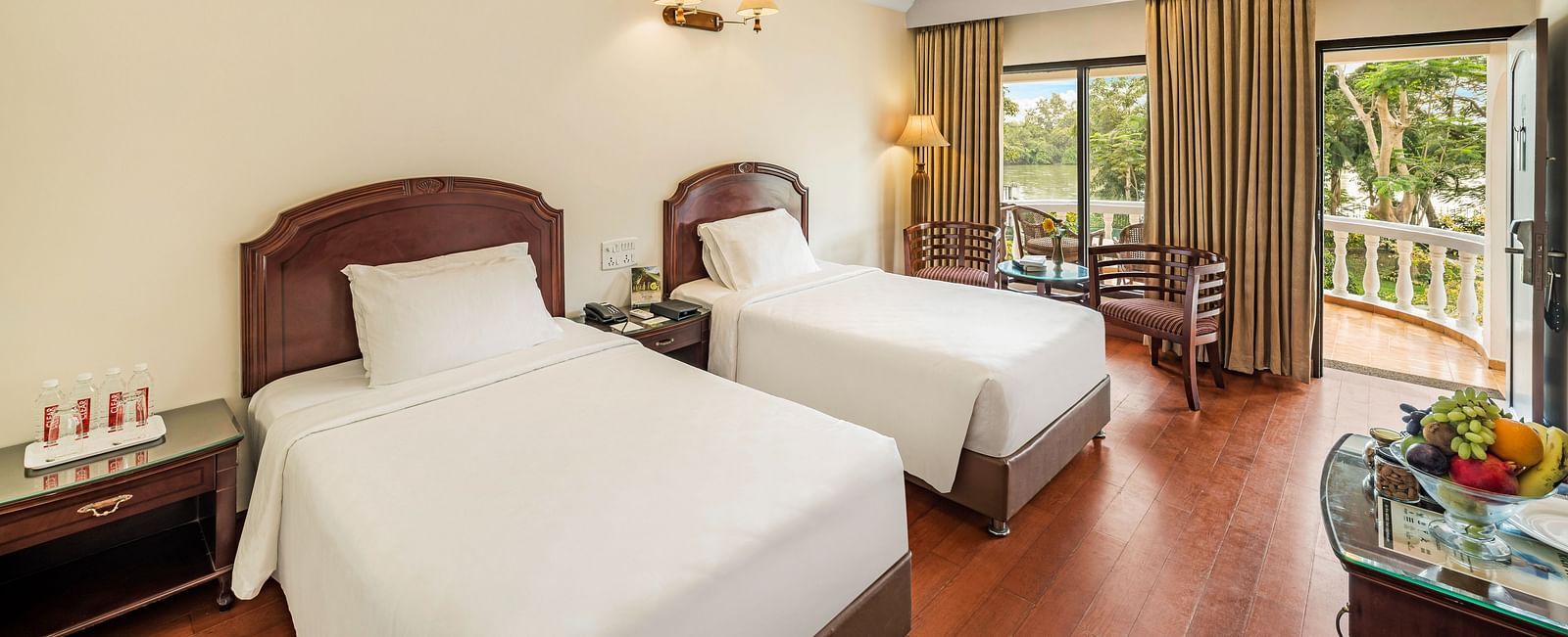 An image of the River View Room With Verandah featuring two single beds, bed side table, lamps, flat screen TV, and chairs - GReaT Trails River View Resort Thanjavur By GRT Hotels