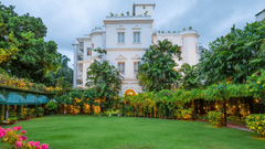 Facade view of Kenilworth Hotel, a city centre hotel in Kolkata, with a lawn in front of it, trees having fairy lights, many trees surrounding the lawn area as seen during twilight hour.
