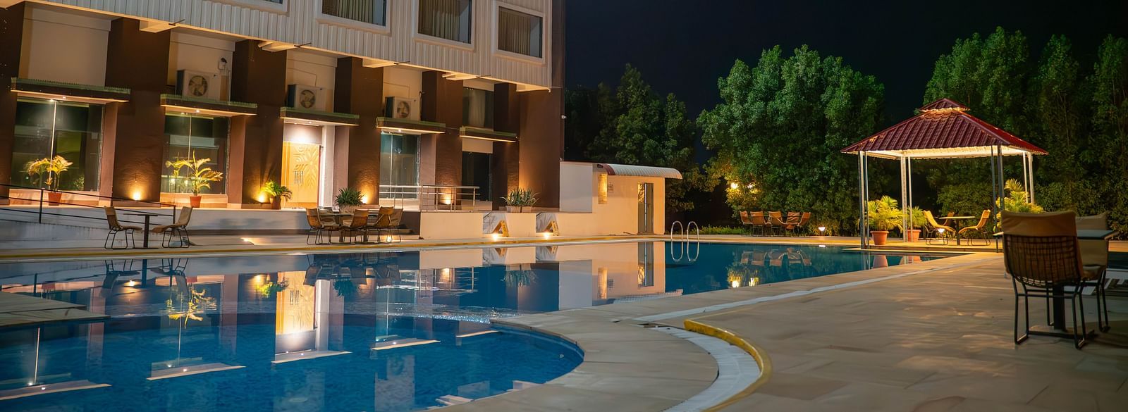Bamboo Saa Mulberry Resort in Pushkar standing tall beside the outdoor swimming pool at night featuring warm lighting and an open gazebo. 