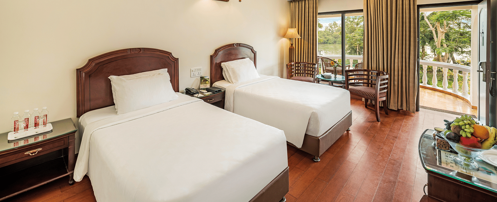 An image of the River View Room With Verandah featuring two single beds, bed side table, lamps, flat screen TV, and chairs - GReaT Trails River View Resort Thanjavur By GRT Hotels